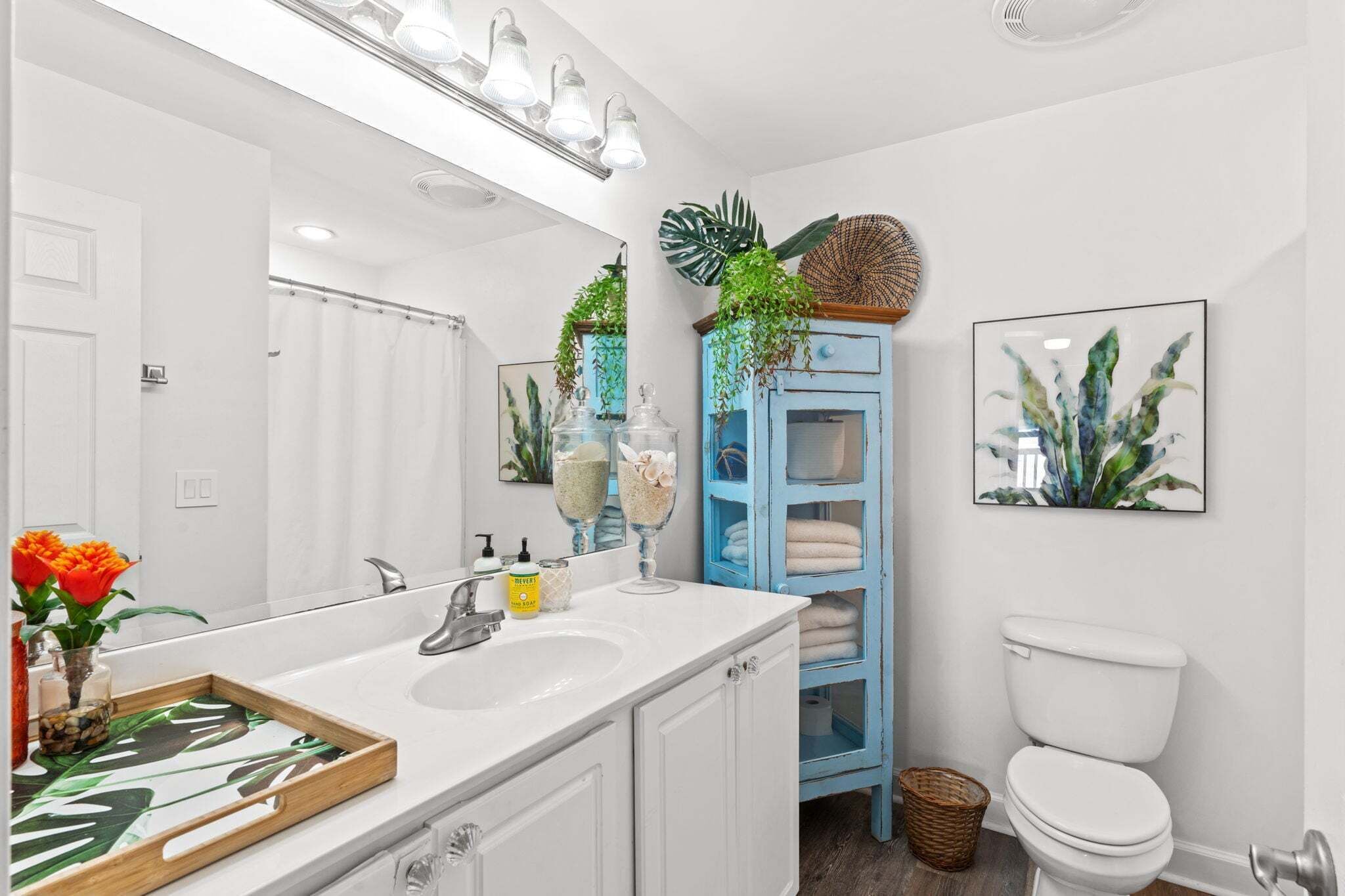 A bathroom with a white sink, a blue cabinet, a toilet, and a shower curtain.