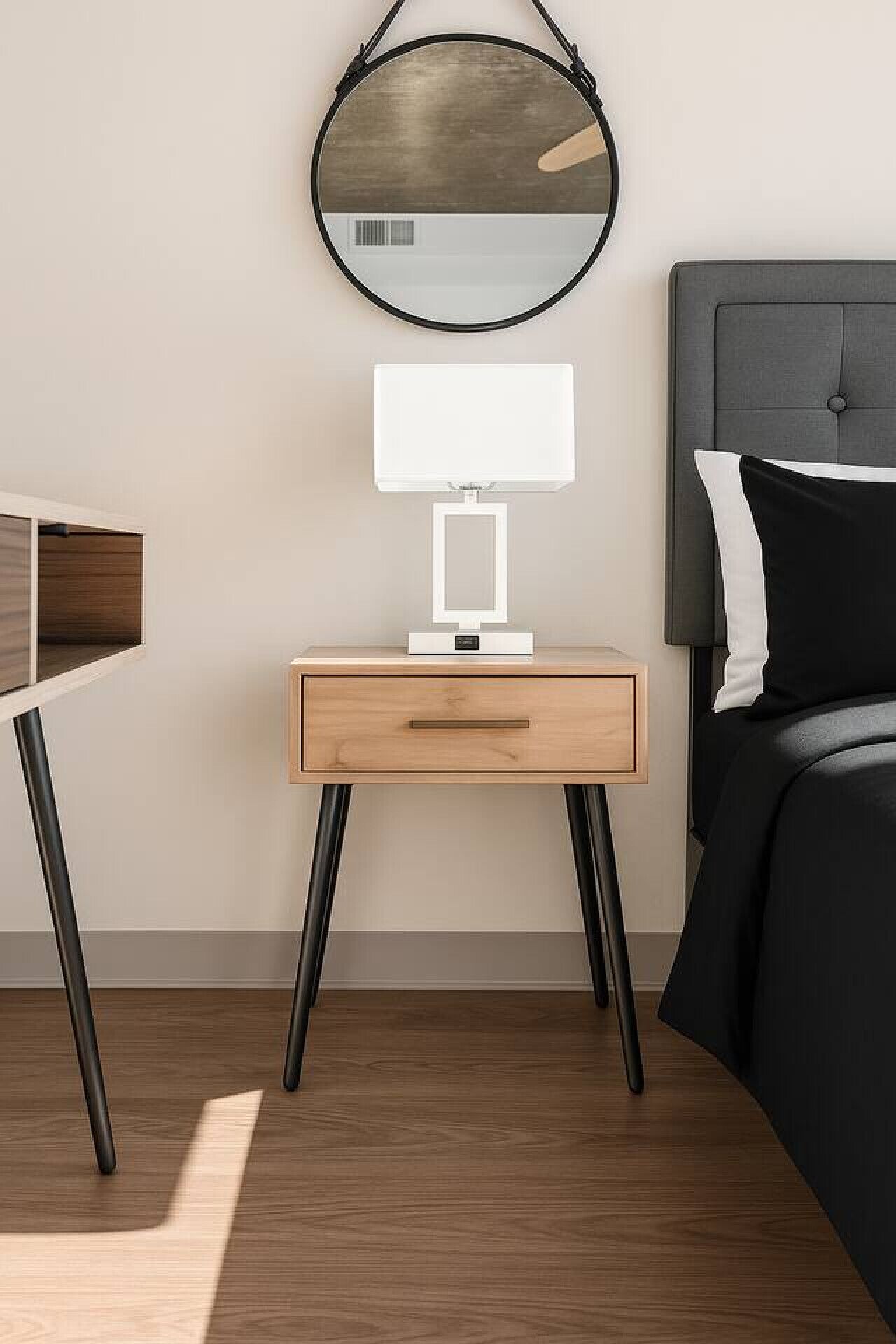A modern bedroom with a bed, bedside table, lamp, and a round mirror.