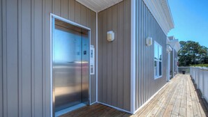 Un bâtiment doté d’une terrasse en bois, d’un ascenseur en métal et d’une rambarde blanche.