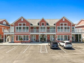 A multi-story hotel with a red facade, balconies, and a parking lot with several cars. - Lucy's Gift: Spacious balcony overlooking the intercoastal waterway (Southport)