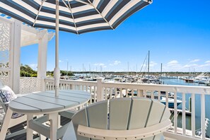 A covered outdoor seating area with tables and chairs, overlooking a marina with boats. - Lucy's Gift: Spacious balcony overlooking the intercoastal waterway (Southport)
