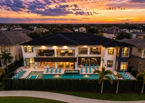 Ein zweistöckiges Haus mit Swimmingpool, Sitzgelegenheiten im Freien und Blick auf den Sonnenuntergang.