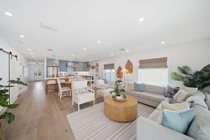 Ein modernes Wohnzimmer mit einer Couch, Sesseln, einem Couchtisch und einer Küche im Hintergrund.