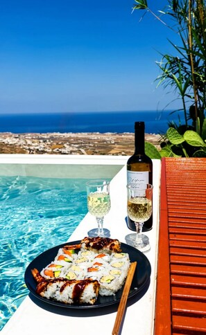 A dining table with sushi, wine, and glasses by a pool with a view of the sea. - Martynou View (Santorini)