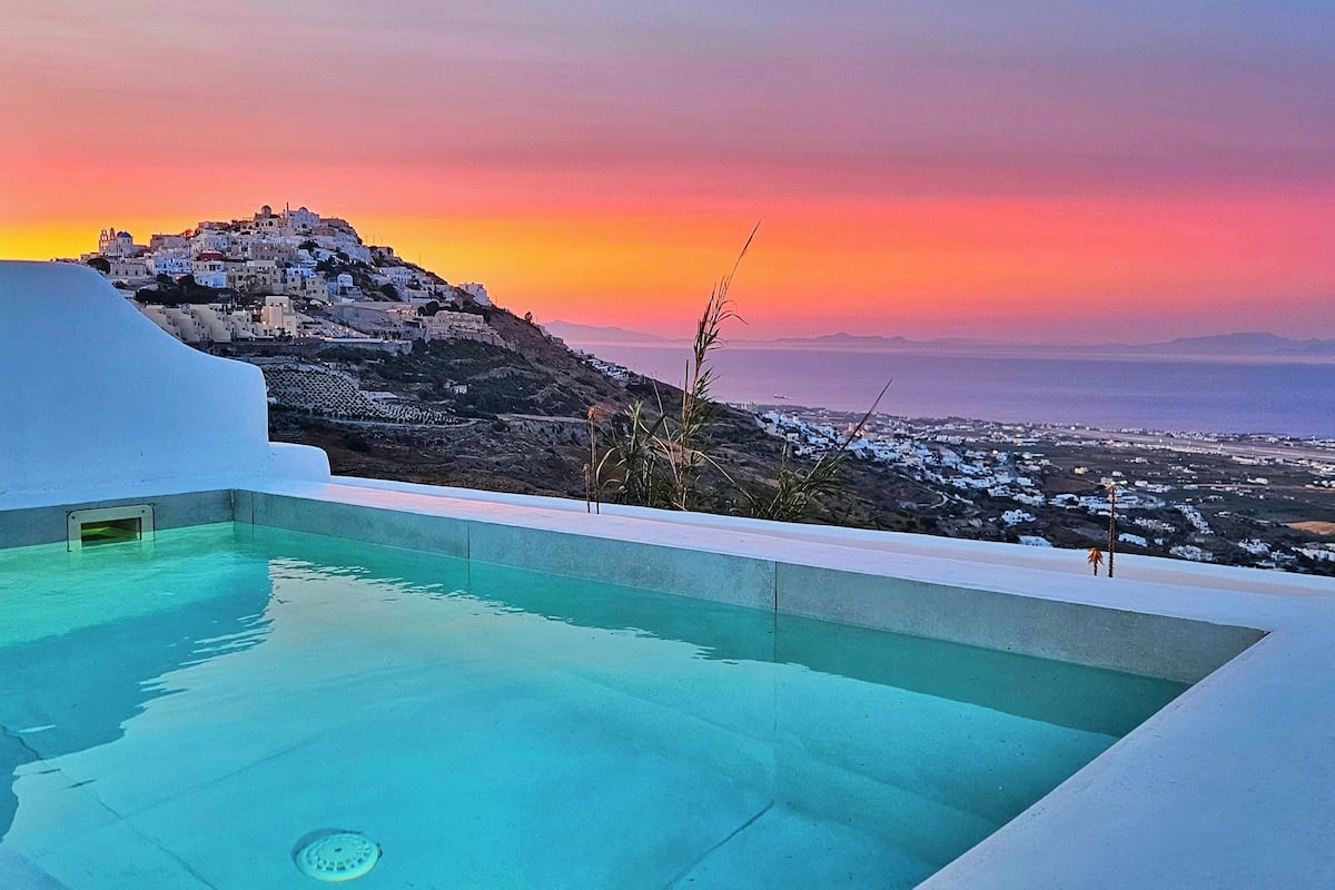 Une piscine offrant une vue sur un village perché sur une colline, au coucher du soleil.
