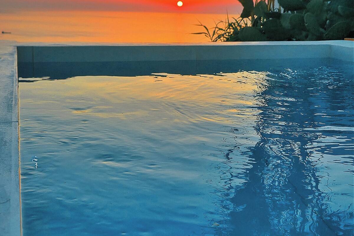 Une piscine offrant une vue sur le coucher de soleil, avec une eau calme et un horizon lointain.
