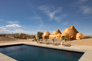 A pool with lounge chairs, a desert landscape, and unique terracotta-roofed buildings.