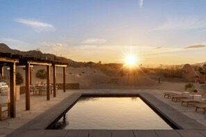 A pool with a pergola and outdoor seating, surrounded by desert landscape and a sunset. - Sandora Domes - Architectural Retreat Near National Park (Joshua Tree)