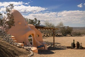 A unique, sculptural building with a curved entrance, outdoor seating, and a pergola.