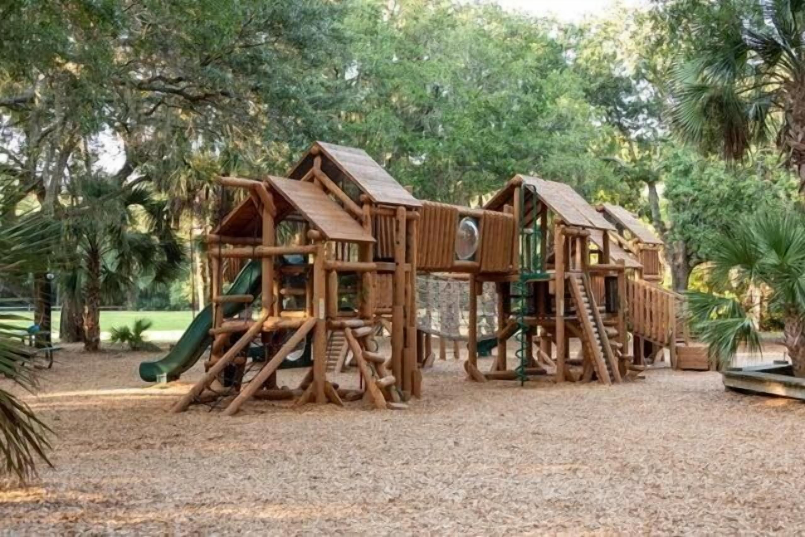 Een houten speelconstructie in een park met een glijbaan en klimelementen.