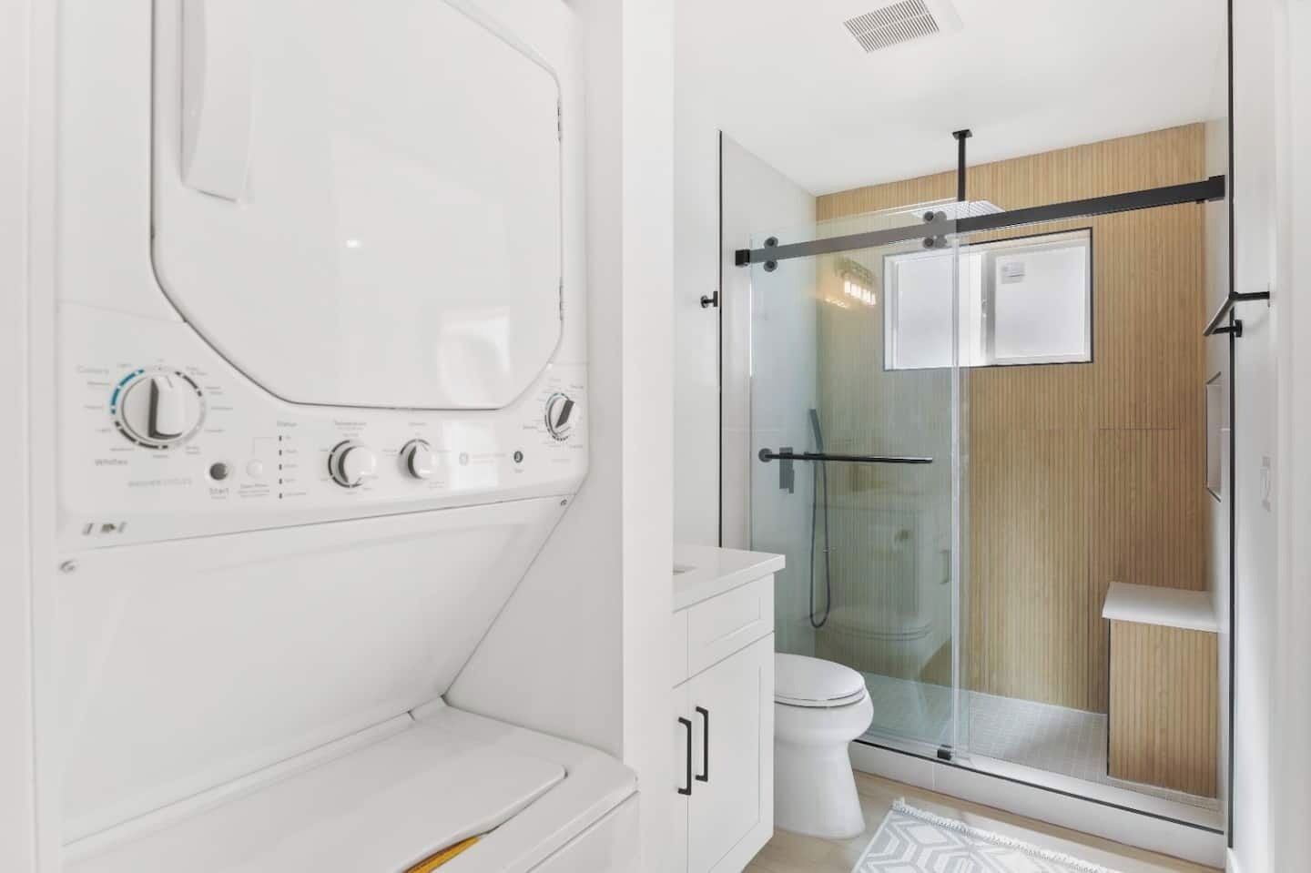 Et moderne badeværelse med bruseniche i glas, et hvidt toilet og en indbygget vaskemaskine.