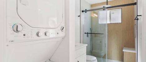 Et moderne badeværelse med bruseniche i glas, et hvidt toilet og en indbygget vaskemaskine.