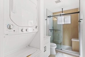 A modern bathroom with a glass-enclosed shower, a white toilet, and a built-in washing machine. - Cozy Luxury Retreat: Near the Beach & Garden Views (San Diego)