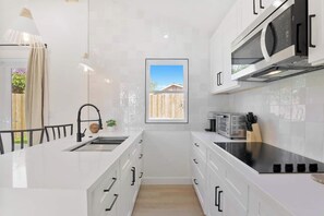 A compact kitchen with white cabinetry, a built-in microwave, and a window with a view of a wooden fence. - Cozy Luxury Retreat: Near the Beach & Garden Views (San Diego)