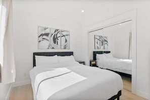 A modern bedroom with a large bed, a nightstand, a mirror, and abstract wall art. - Cozy Luxury Retreat: Near the Beach & Garden Views (San Diego)
