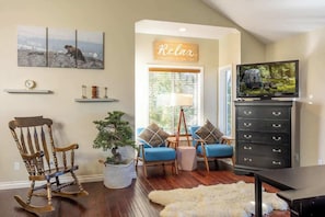 A living room with a wooden rocking chair, blue sofas, a television on a black cabinet, and a painting on the wall. - Lakeview Lodge,HotTub, FirePit, BBQ, firework view (Big Bear Lake)