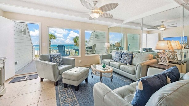 A spacious living room with a view of the ocean, a ceiling fan, and a large mirror reflecting the room. - Gulfside Gem 144-Gulf Views-Sleeps 6 (Panama City Beach)