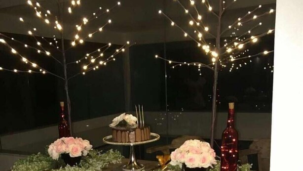Une table en bois sur laquelle se trouvent un gâteau, deux bouteilles et des compositions florales.