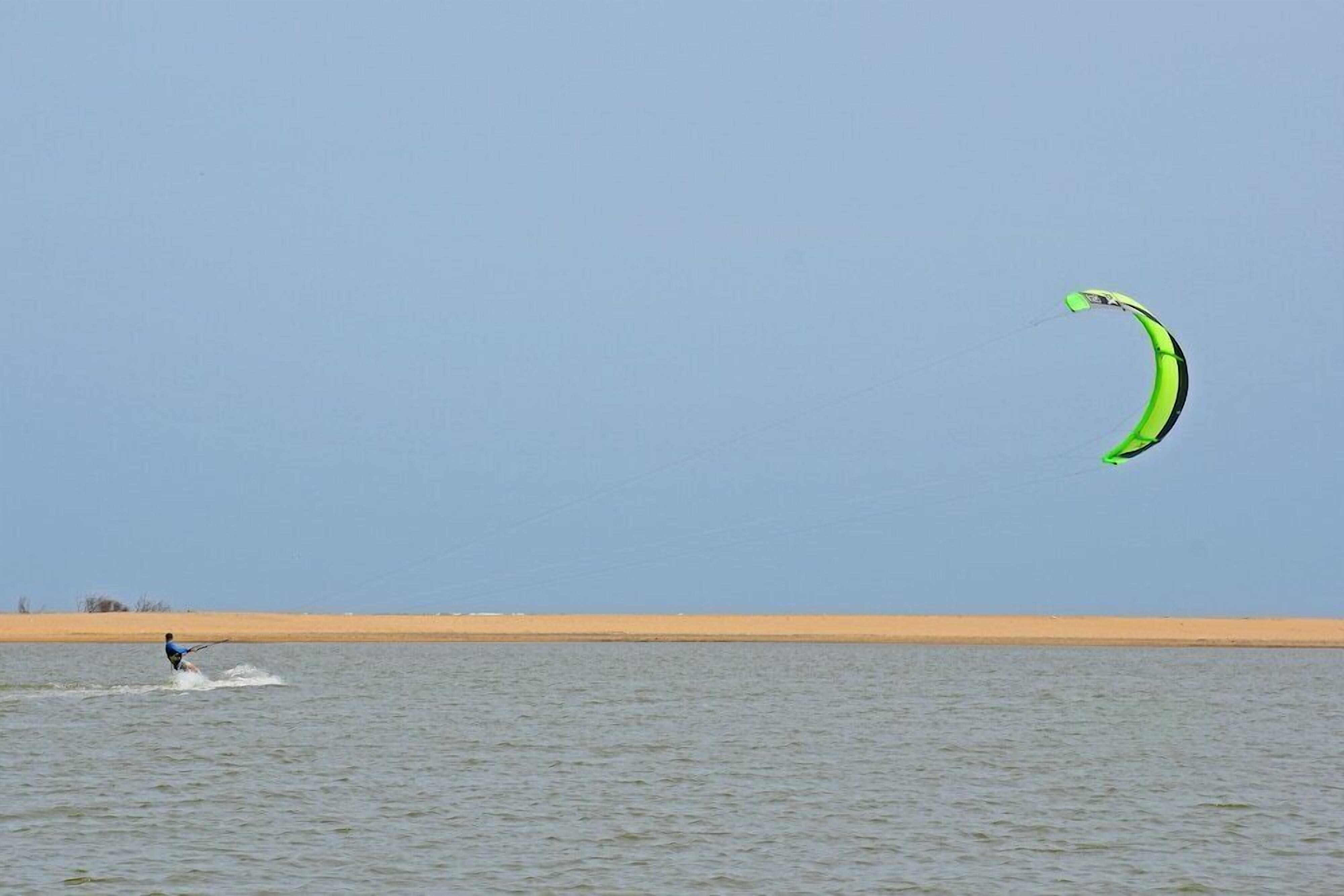 A person water skiing with a green kite on a clear day.