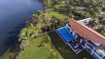An aerial view of a resort with a swimming pool, palm trees, and a body of water.