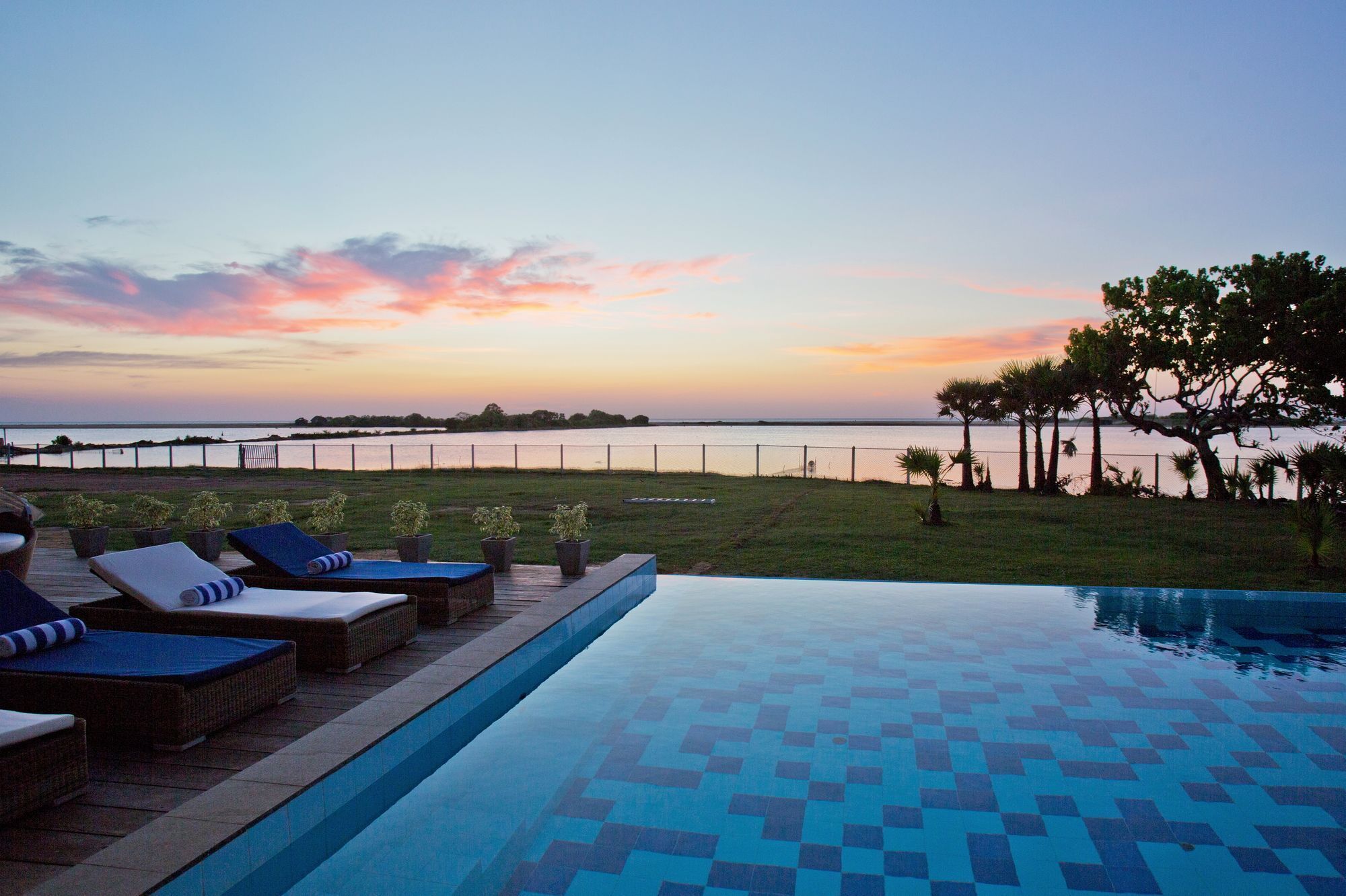 A pool area with lounge chairs, a view of the water, and a sunset.