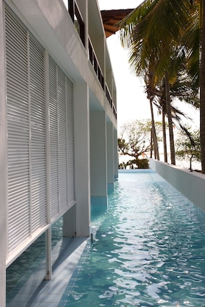 Une vue sur la piscine, avec un bâtiment blanc, des palmiers et une piscine à l’eau d’un bleu limpide.