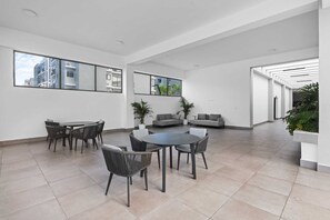 A spacious living area with a round table and chairs, a sofa, and large windows offering views of buildings. - ARG Tropical Home/ Swimming Pool, Fitness Center (Punta Cana)