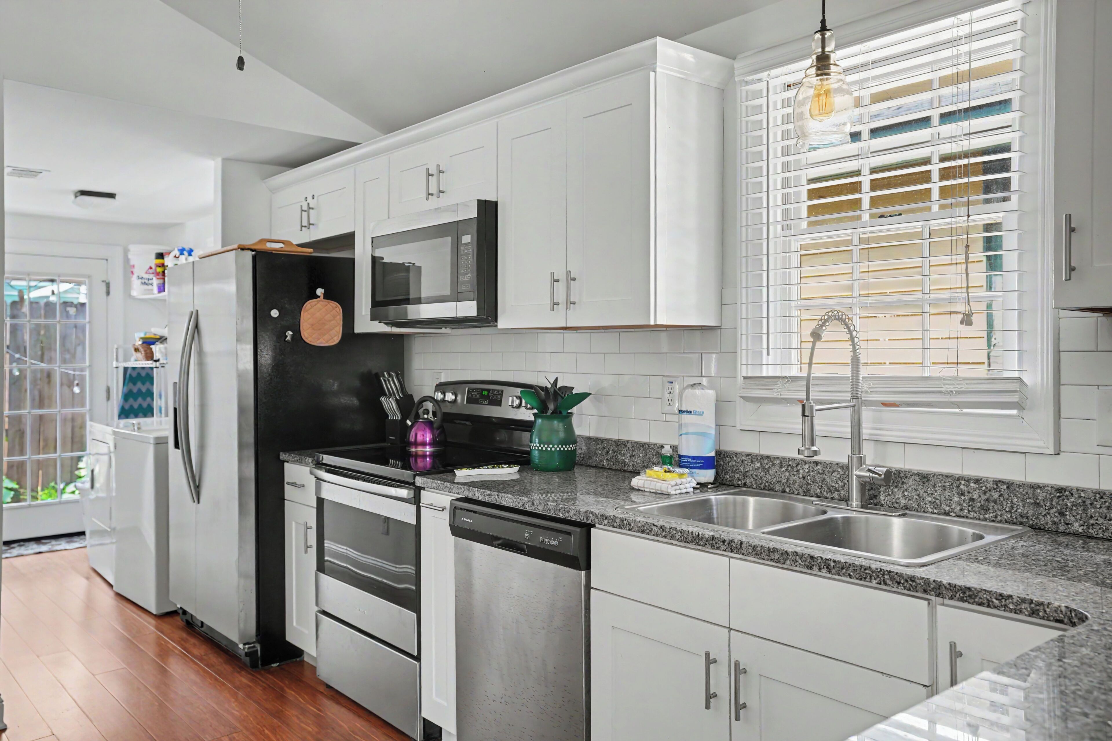 A modern kitchen with white cabinets, a stainless steel dishwasher, a microwave, and a granite countertop.