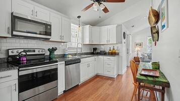 A kitchen with white cabinets, stainless steel appliances, a wooden dining table, and a ceiling fan.