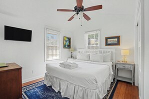 Ein Schlafzimmer mit einem Bett, Deckenventilator, Fernseher, zwei Nachttischen und einem Beistelltisch.