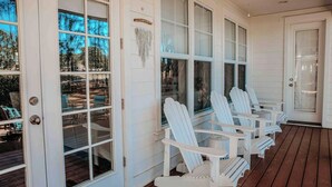 A covered porch with white Adirondack chairs, large windows, and a wooden deck. -    🦩Book Me Baby! Cottage By The Sea at Sandestin Resort~Golf Cart🦩 (Miramar Beach)