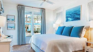 A bedroom with a large bed, a nightstand, a desk with a lamp, and a window with curtains. - 🦩Book Me Baby! Cottage By The Sea at Sandestin Resort~Golf Cart🦩 (Miramar Beach)