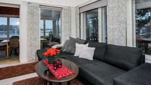 A living room with a dark grey sofa, a round coffee table with a red placemat, and a vase with red flowers.
