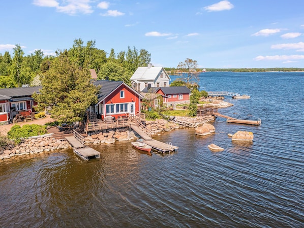 Järvenrantatontti, jossa on laiturissa olevia veneitä, puinen laituri ja punainen rakennus.