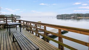 A wooden deck with benches overlooking a calm body of water, a distant shoreline, and a clear sky.