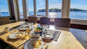 A dining table with plates of food, glasses, and cutlery, set against a backdrop of a lake view through large windows.