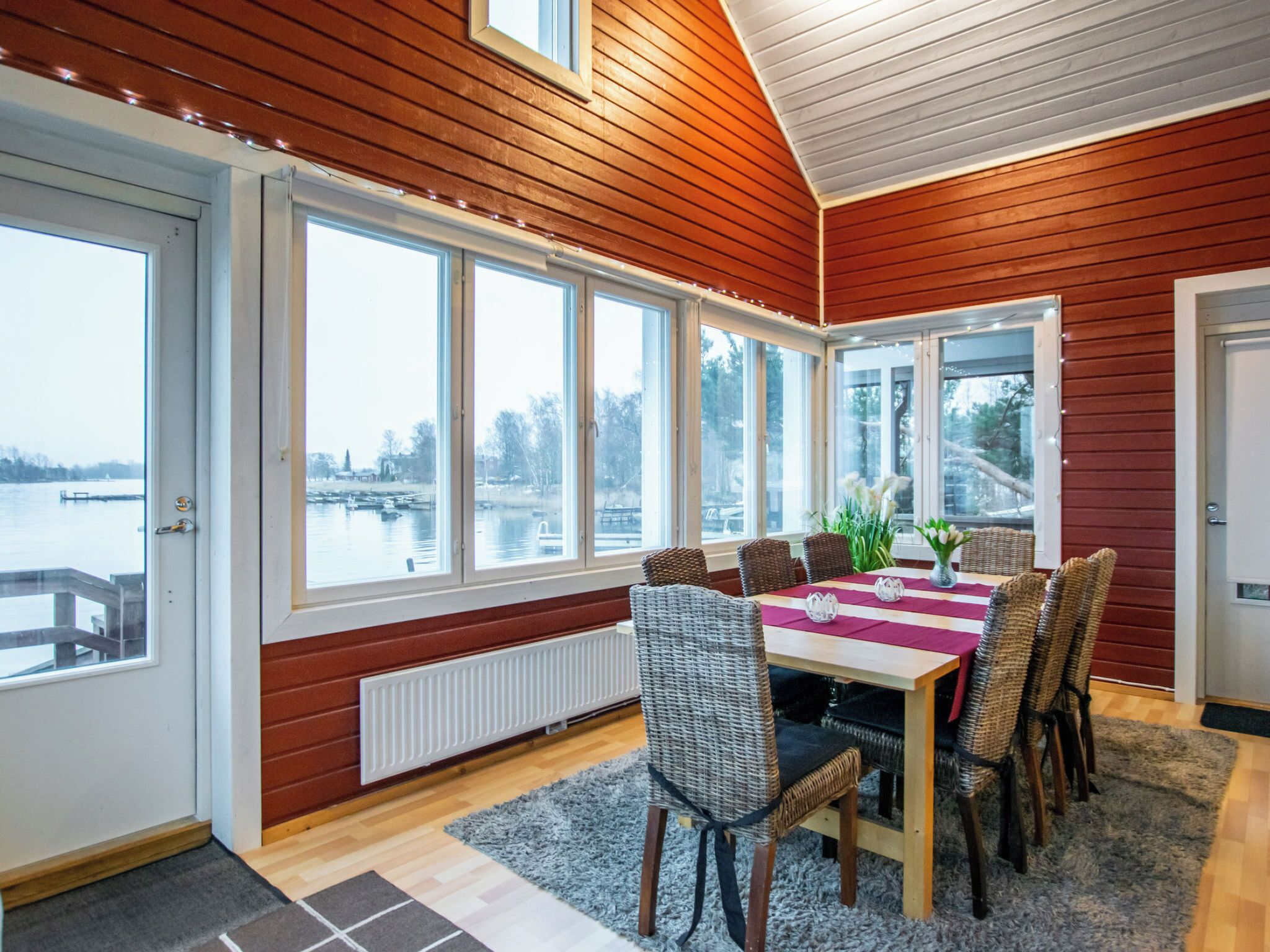 En matplats med ett bord dukat för sex personer, stora fönster och utsikt över en sjö eller ett annat vattendrag.