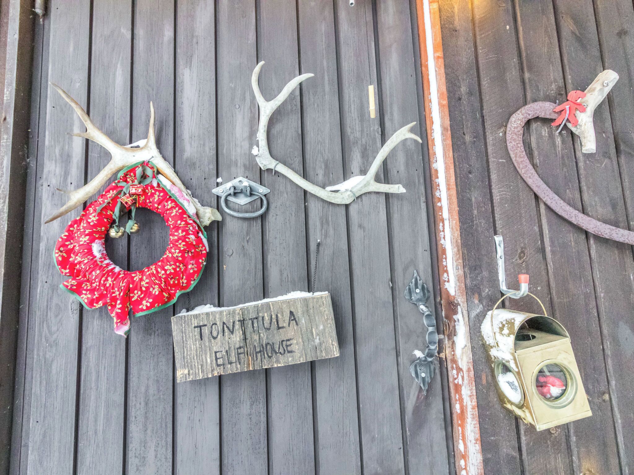 A wooden surface with a red wreath, antlers, a metal bell, a sign reading 'TONITULA ELPH HOUSE,' and a small birdcage.