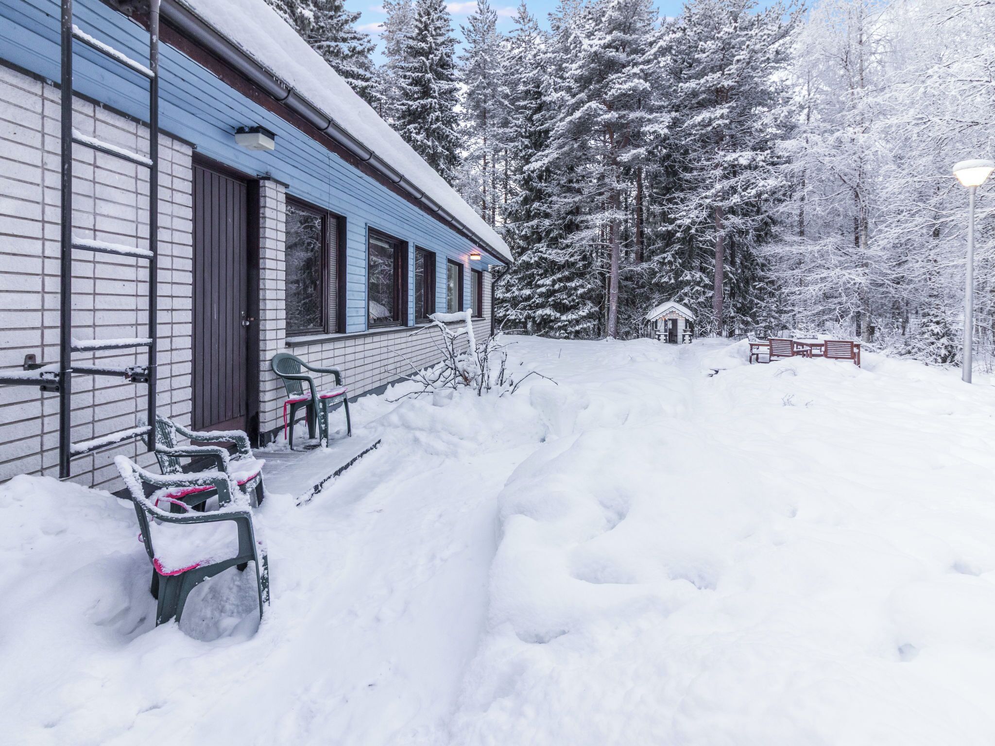 A snow-covered outdoor area with a building, a small cabin, and snow-covered trees.