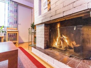 Una chimenea con protector, una silla de madera, una mesita y un tapete rojo en una habitación con pared de ladrillo.
