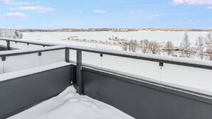 A snow-covered balcony with a view of a frozen landscape and distant buildings.