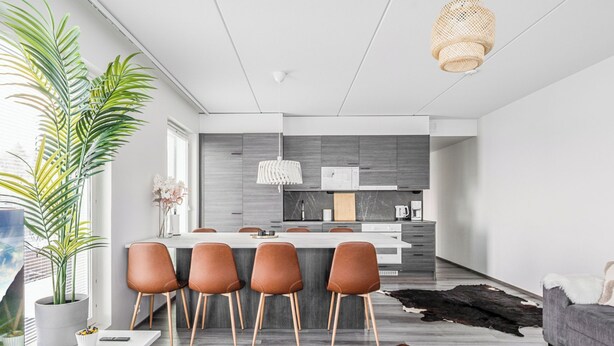 A modern kitchen with a central island, wooden chairs, and a cowhide rug.