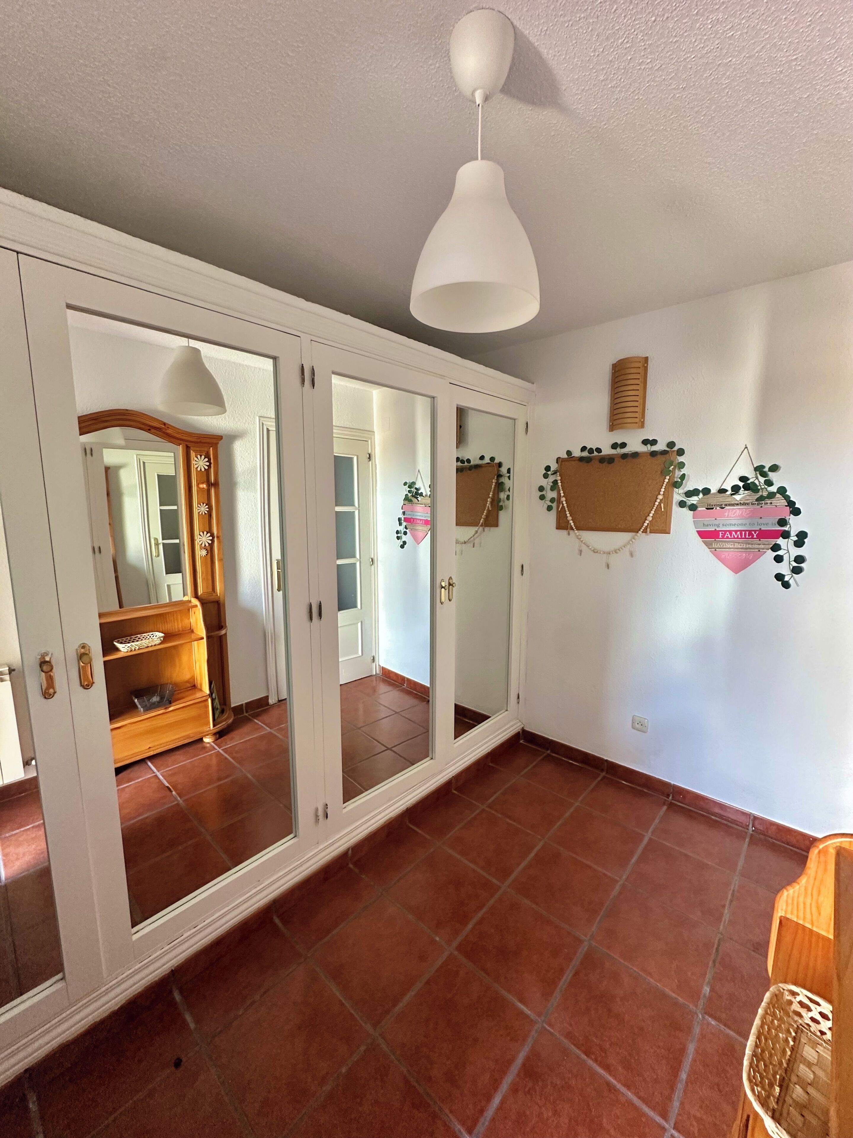 Una habitación con un armario espejo, una lámpara colgante y un adorno en la pared.