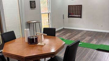 Un coin repas avec une table ronde en bois, des chaises noires, un ventilateur de plafond et un tapis vert sur le sol.