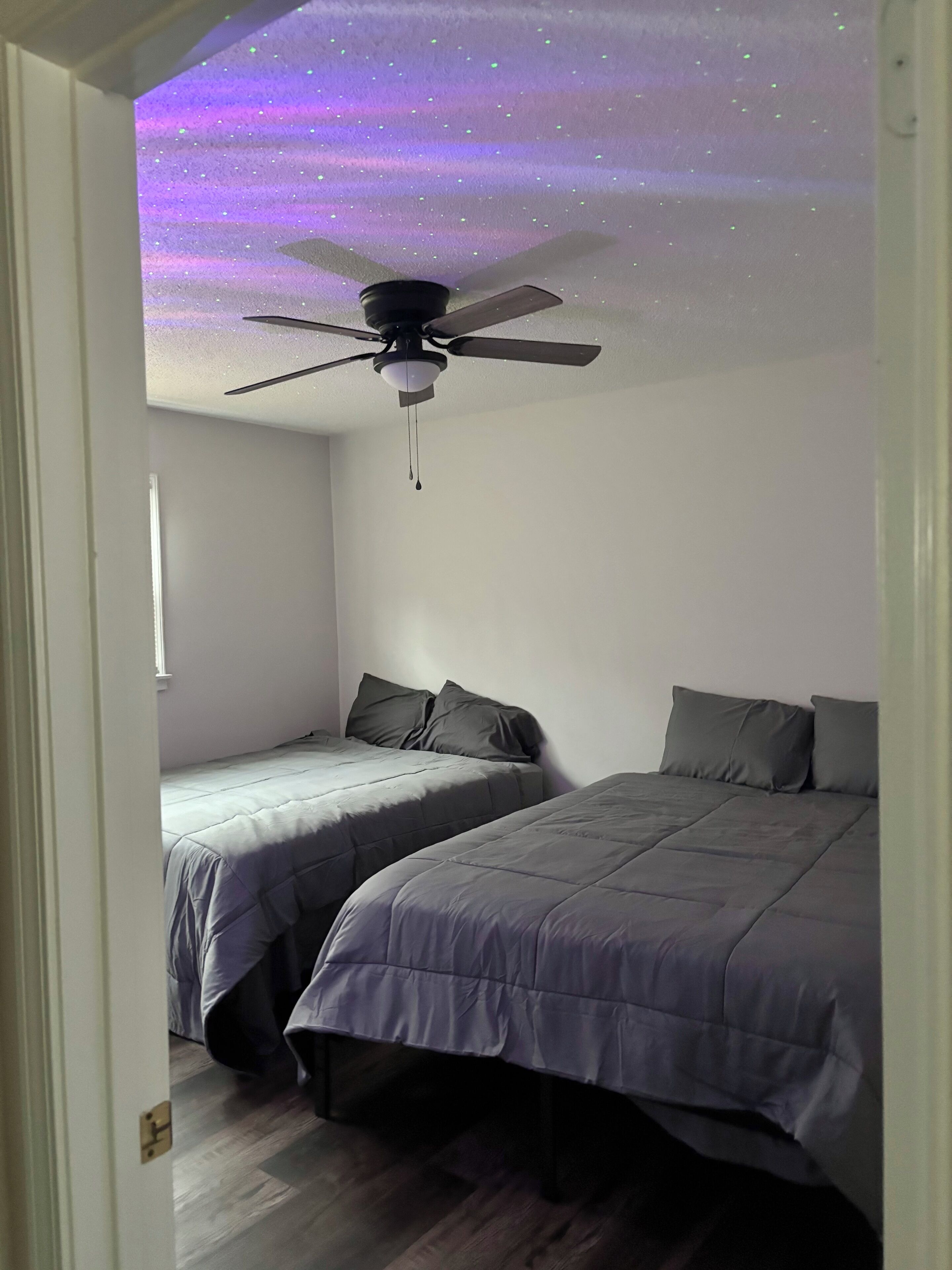 Un dormitorio con dos camas, ventilador de techo y proyección de cielo estrellado.