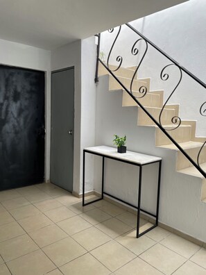 Eine Treppe mit Metallgeländer, ein kleiner Tisch mit Pflanze und eine Tür in einem Raum mit Fliesenboden.