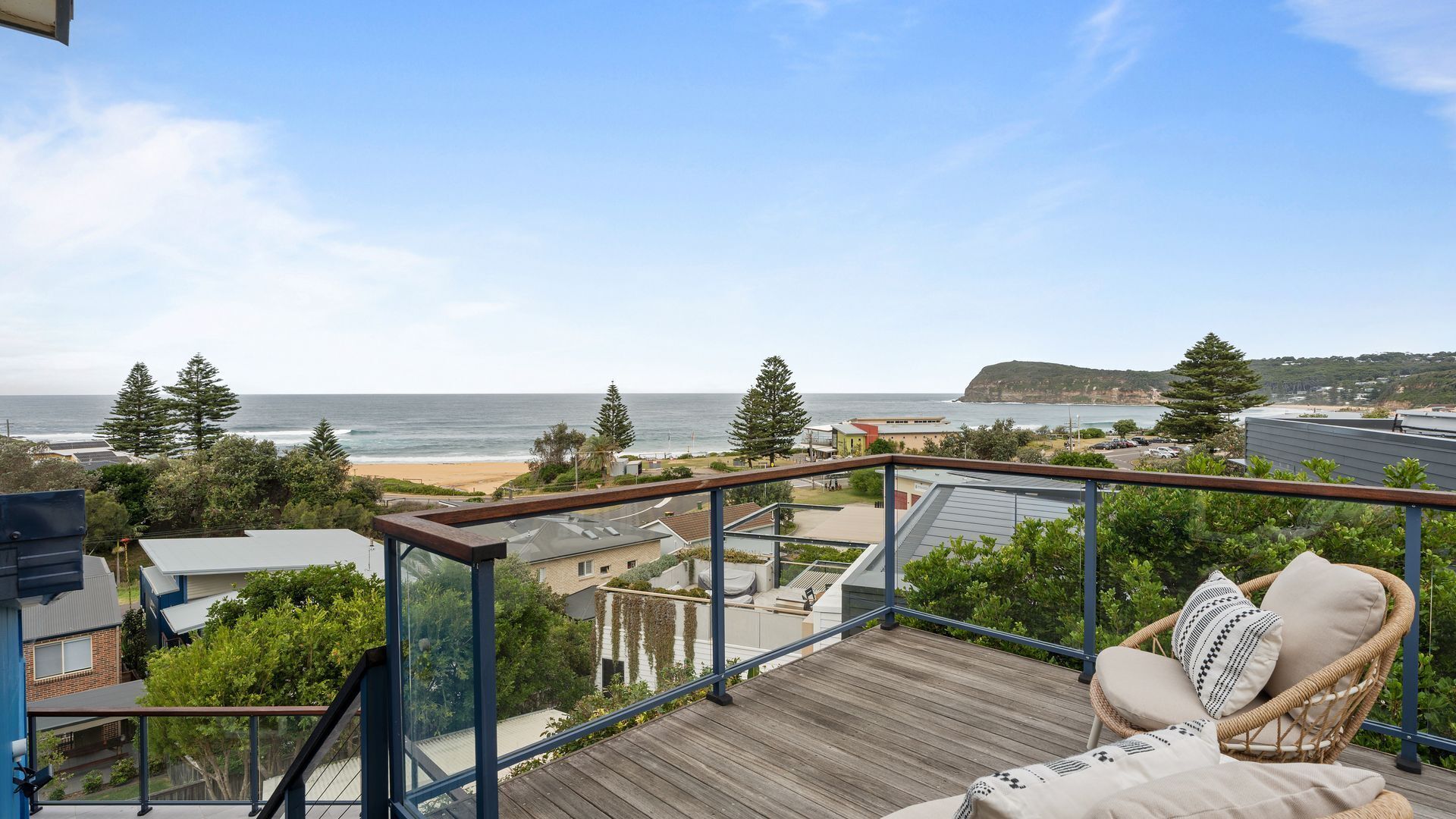 Ein Balkon mit Blick auf den Strand, ein Korbstuhl und eine Holzterrasse.