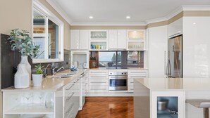A modern kitchen with white cabinetry, a stainless steel oven, and a large window. - Copa Panorama House Stay (Copacabana)