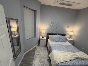 A bedroom with a bed, two bedside tables with lamps, a large mirror, a window with blinds, and a wall decoration. - Cozy 1-bedroom apartment in delightful Newark with AC (Newark)