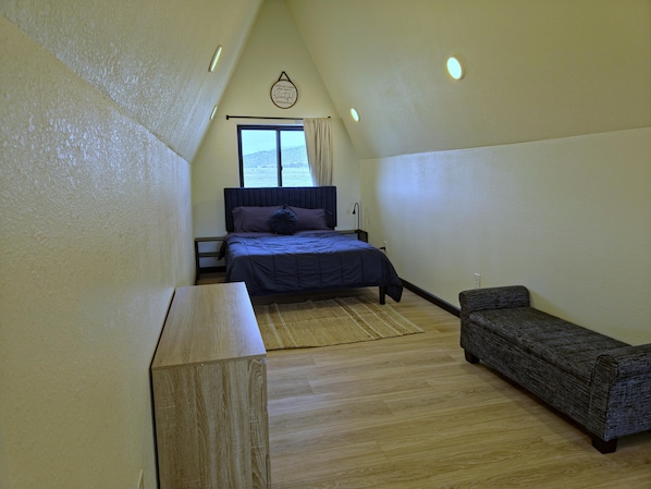 A bedroom with a bed, a nightstand, a bench, a window, and a ceiling light fixture.